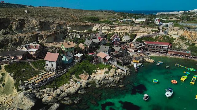 Aerial view of Popeye Village, Malta. Colorful seaside cottages, turquoise waters, and coastal scenery create a charming and playful Mediterranean landscape from above