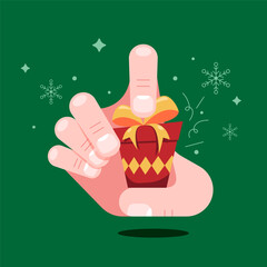 Hand holding a small red Christmas gift box with gold ribbon on green background with snowflakes