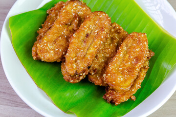 Crispy Thai fried bananas with sesame seeds served on a banana leaf in a white plate, Fried bananas is a traditional Asian snack with sweet, crunchy texture. Top view close-up shot