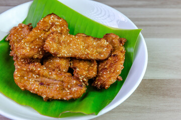 Crispy Thai fried bananas with sesame seeds served on a banana leaf in a white plate, Fried bananas is a traditional Asian snack with sweet, crunchy texture. Top view close-up shot, copy space