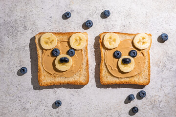 Creative bread slices decorated as cute bear faces with fruit on a light gray countertop