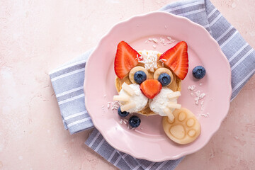 Creative breakfast idea featuring a cat face made from fruit and pancakes on a pink plate
