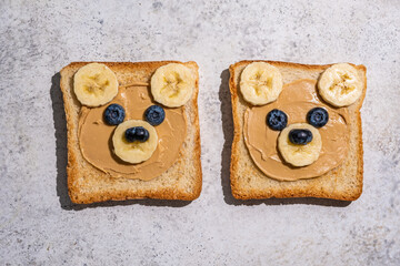 Creative bread slices decorated as cute bear faces with fruit on a light gray countertop