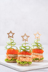 Creative holiday-themed finger sandwiches shaped like Christmas trees with salmon, cucumber, and lettuce on a serving platter