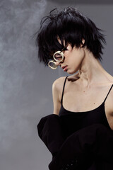 Fototapeta premium Stylish young woman with short black hair wearing glasses and a black top in a smoky atmosphere