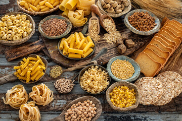 Different types of uncooked pasta on rustic wooden table, in the spoons, cutting board and bowls 