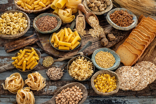 Different types of uncooked pasta on rustic wooden table, in the spoons, cutting board and bowls