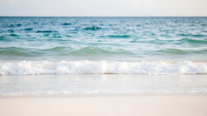 Obraz premium Calm blue ocean waves gently rolling onto a white sandy beach, evoking tropical serenity.