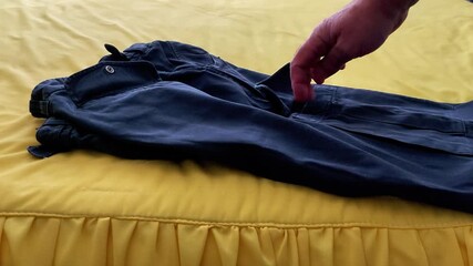 Hand gestures toward neatly folded pants resting on a textured yellow ruffled bedspread, highlighting tactile detail and everyday home life in a clean, visually engaging setup