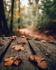 Fototapeta premium Dry autumn leaves scattered across a weathered wooden surface with a misty forest path behind.
