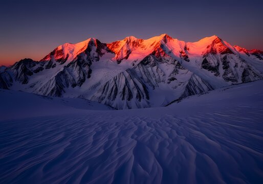 Snow-covered mountain peaks illuminated by alpenglow at dawn