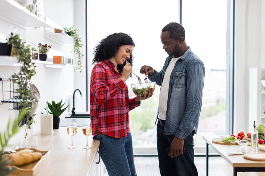 A diverse couple shares a salad in a bright, modern kitchen, enjoying a moment of togetherness and healthy eating.