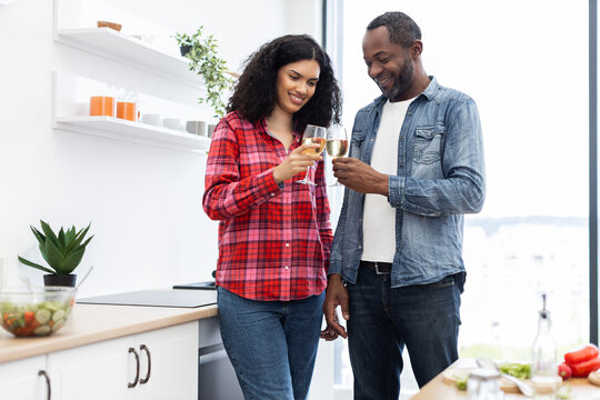 A smiling couple clinks glasses of wine in a modern kitchen, celebrating a special moment together.