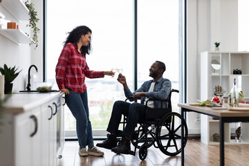 A diverse couple celebrates with wine in a bright, modern kitchen. One partner is in a wheelchair.