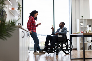 A diverse couple enjoys a celebratory moment in a bright, modern kitchen, with one person in a wheelchair.