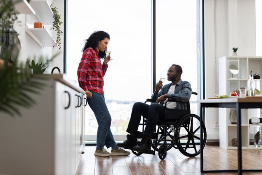 A couple enjoys wine in a modern kitchen, with one person in a wheelchair.