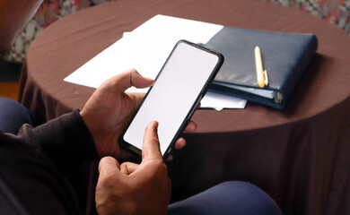 Close Up of Smartphone with white Screen Mock Up Display In Male Hands. Man Sitting In Home Browsing Internet , Watching Content, News, Financial Reports on Phone. 