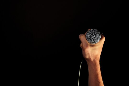 Hand holding microphone against black background