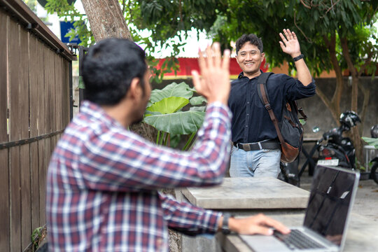 Two Asian men greeting each other with a cheerful high-five outdoors
