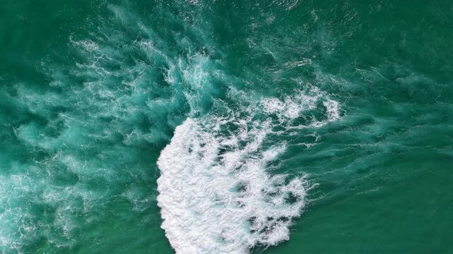 Aerial view of powerful ocean wave breaking in turquoise sea, creating dynamic splash pattern in clear coastal waters
