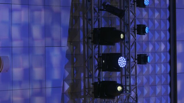 Blue stage lights illuminate metal truss rig against patterned wall, creating dramatic concert event atmosphere