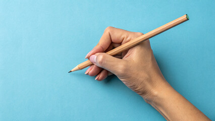 Top close up pov above overhead view  of hand holding wooden pencil starting to draw a picture isolated over blue pastel color background