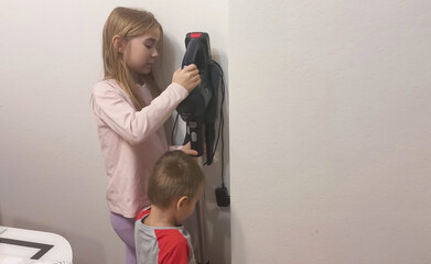 A girl and a boy hang a vacuum cleaner on a base