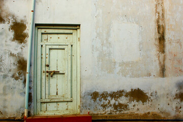 Old rustic wooden door on a weathered wall in Saurashtra, India. Faded paint, peeling texture, and vintage architecture create a nostalgic rural feel.