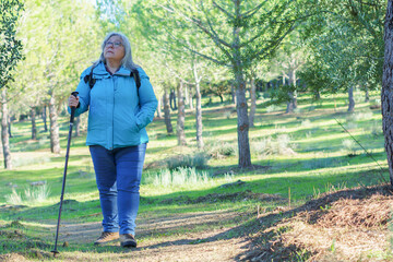 Senior woman walking in a pine forest, enjoying an active outdoor lifestyle, looking up with a thoughtful expression