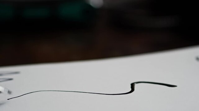 Calligraphy artist uses black ink dipper pen to draw stylised letter scroll