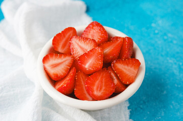 bowl of fresh sliced strawberries on blue background with white napkin