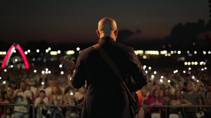 A Bald Guitarist In A Suit Plays For A Crowd Holding Phone Lights. A Musician Performs On Stage During A Night Concert.
