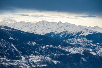 Panorama hivernal des Alpes avec chaîne de montagnes enneigées. Ciel nuageux dramatique, ambiance...