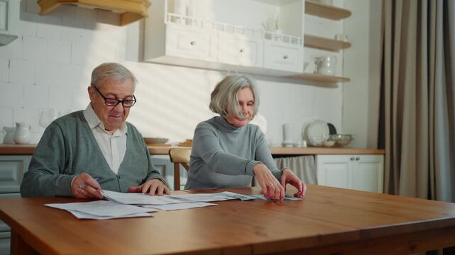 Old woman and man counting income and expenses, cash dollars and utility bills. Portrait of positive married couple at home kitchen in weekend, man and woman planning family budget, finance problems