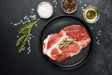 Raw beef steak with herbs and seasonings on black plate