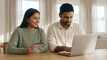 Indian couple sitting at the dining table with a laptop and credit card in hand, doing online shopping.