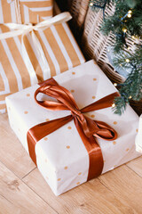 Wrapped presents with ribbon under Christmas tree with lights, festive holiday gifts on floor.