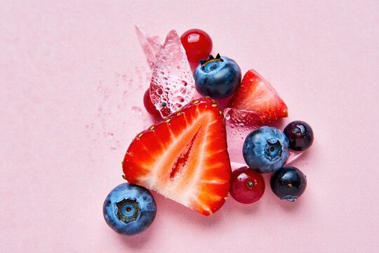 Strawberry slice and blueberries burst on pink background with splash effects - Powered by Adobe