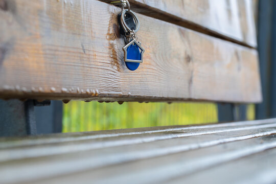Metal keychain with a house-shaped keyring and an intercom key on a bench made of dark wooden planks in a park