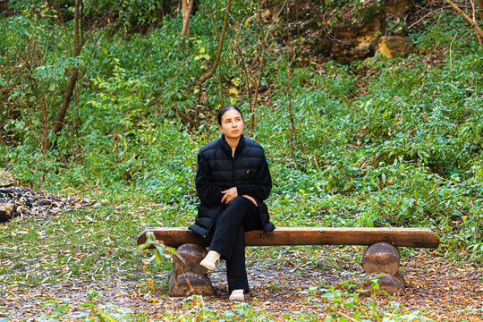 Young beautiful brunette student sit on the banch with laptop under blooming sakura