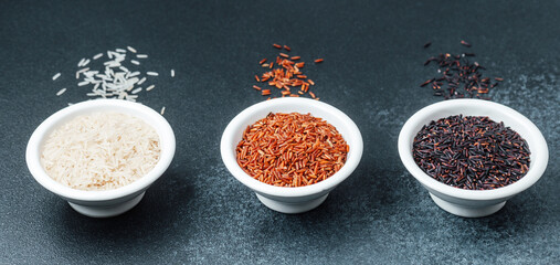 Three ceramic bowls with rice on dark background with scattered grains