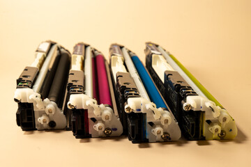 Four color printer cartridges arranged in a row on a beige background represent printing supplies,...