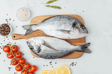 Raw dorado fish with ingredients on wooden cutting board over white background