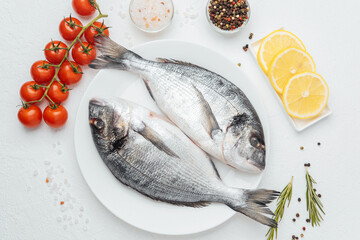 Close up of two dorado fish on white plate with lemon and tomato