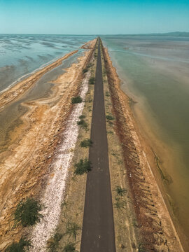 Aerial view of a long straight road cutting through the salt flats and coastal landscape of Kutch, with contrasting earth textures and shallow waters on both sides.