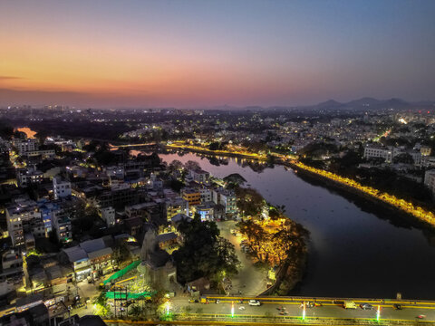 Aerial view of the Godavari River in Nashik during sunset, with glowing city lights, reflections on the water, and the skyline fading into colorful evening hues.