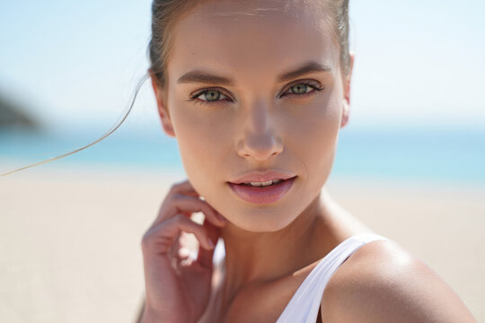Sun-washed close-up portrait of a woman with green eyes and glowing skin at beach