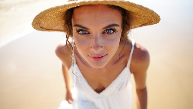 Close-up of a barefoot woman in a sunlit straw hat standing on sandy beach - Powered by Adobe