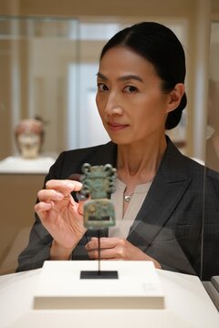 Art curator examines a small ancient artifact in a museum display case.