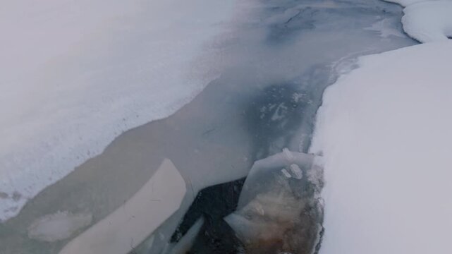 The forester walks on the thin ice of the river and breaks it with his feet. Winter hiking by the shore of a frozen river. A dangerous walk. From the first person.